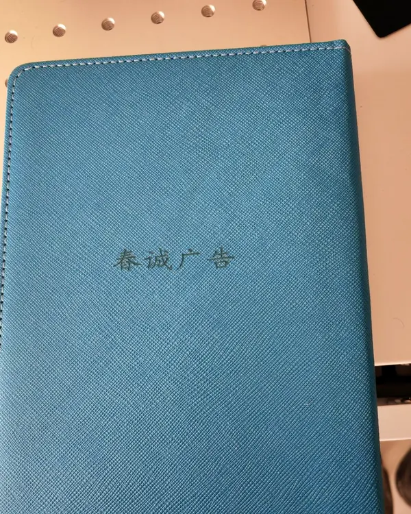 合肥激光打标代工实拍 · 深蓝色荔枝纹皮革笔记本封面激光雕刻「春诚广告」字样，凹痕均匀无焦边