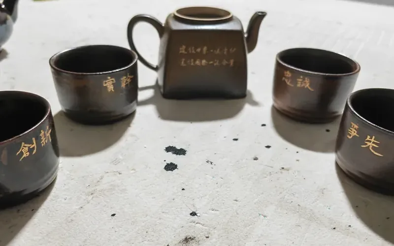 合肥激光打标代工实拍 · 紫砂茶具一套四杯激光刻字「实干 忠诚 创新 争先」，壶身刻小字落款，字口深浅均匀、釉面不崩裂