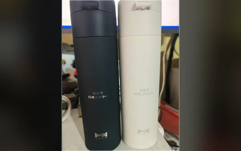 合肥激光打标代工实拍 · 黑色与米白色不锈钢保温杯曲面激光打标「安徽省病理会诊中心」，深色杯打浅字、浅色杯打深字，弧面不变形不起皮